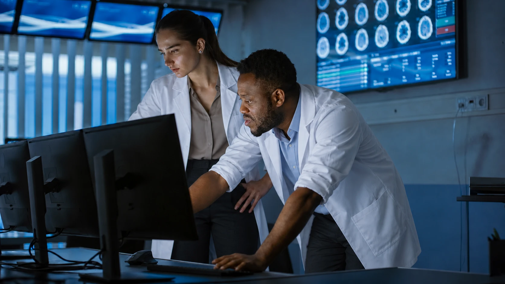 Two researchers in lab coats reviewing brain scan data on monitors